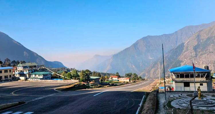 Vue de la piste de l'aéroport de Lukla et des bâtiments terminaux encadrés par des montagnes vertes escarpées sous un ciel dégagé.