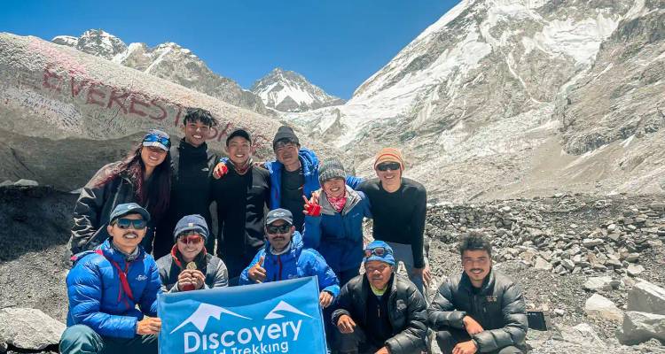 Un grand groupe de trekkeurs posant avec une bannière Discovery à côté du rocher du Camp de Base de l'Everest et de la toile de fond glaciaire.