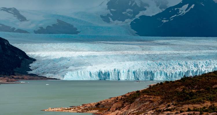 Une vue époustouflante du glacier Perito Moreno avec un décor de montagnes en arrière-plan et de l'eau au premier plan.