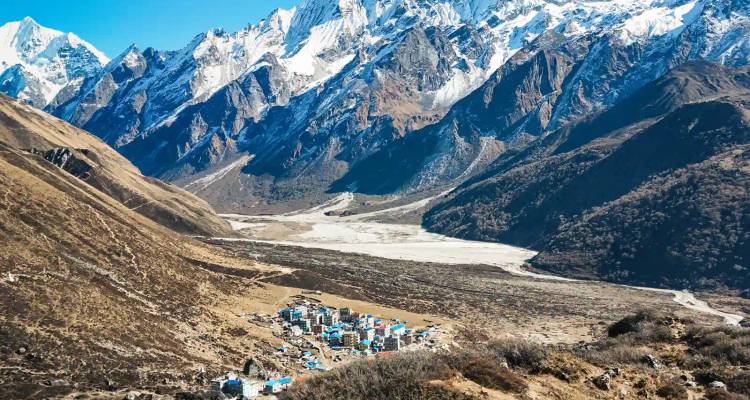 Uitgestrekt uitzicht over de vallei met een klein dorpje dat wordt overschaduwd door met sneeuw bedekte Himalaya-toppen.
