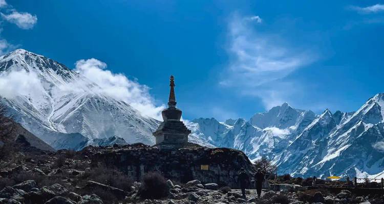 Stenen stupa staande op rotsachtig terrein met op de achtergrond sneeuwwitte Himalayapeïken en een diepblauwe lucht.