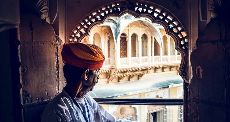Man in traditional attire looking out from a carved window.