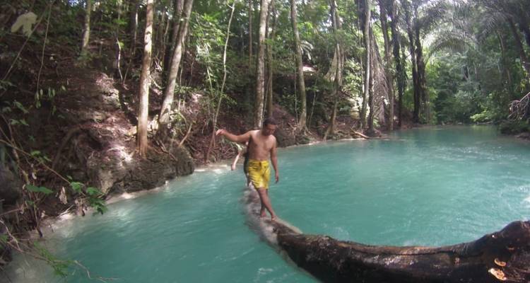 Eine Person, die auf einem Baumstamm über einem türkisfarbenen Wasserbach balanciert.
