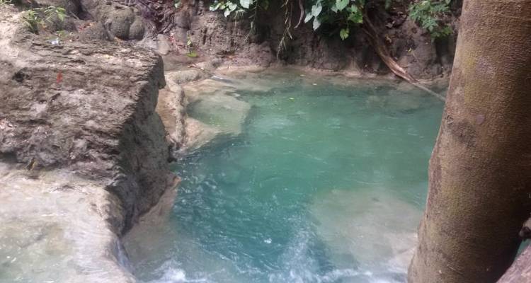 Ein kleiner türkisfarbener Pool, umgeben von Felsen und Wald.