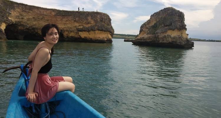Woman sitting on a boat with rocky outcrops in water.