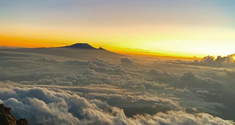 Sunrise view from above the clouds with distant mountain peak.