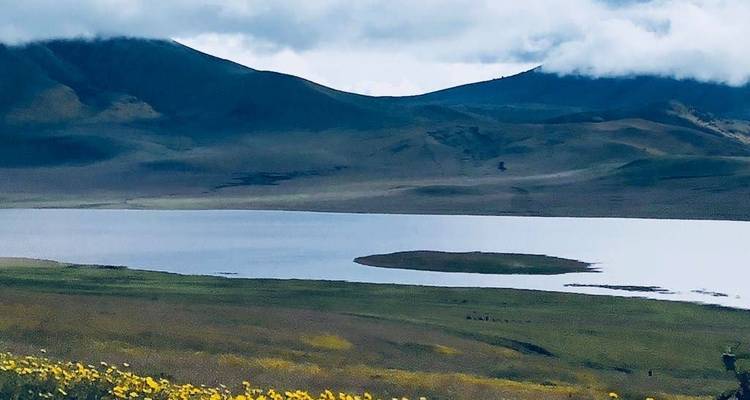 Landschap met een meer en bergen op de achtergrond onder bewolkte luchten.
