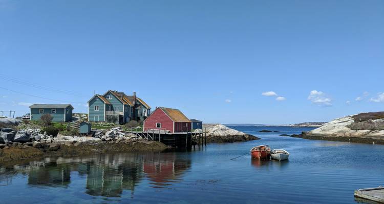 Maisons côtières colorées et petites embarcations se reflétant dans une crique calme par une journée claire.