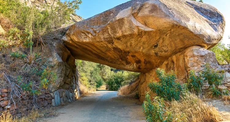 Eine schmale Straße führt unter einer riesigen Granitplatte hindurch und bildet einen natürlichen Tunnel inmitten trockener Vegetation.
