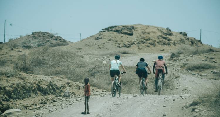 Cyclists riding on a dirt road with a small child standing nearby.