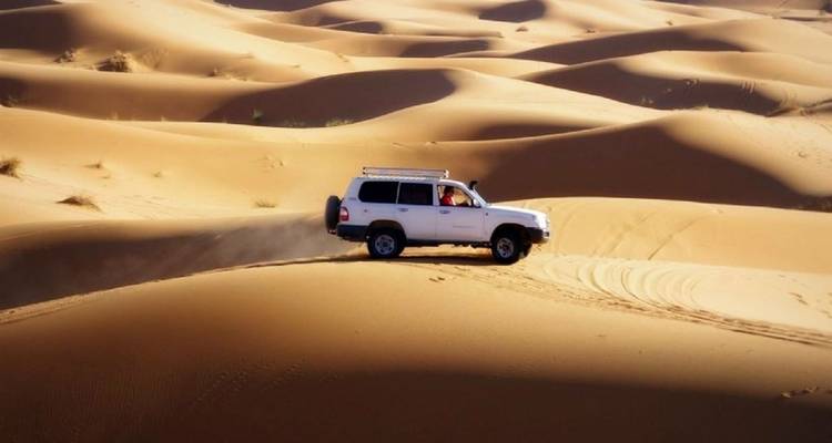 Een witte SUV die door zandduinen rijdt.