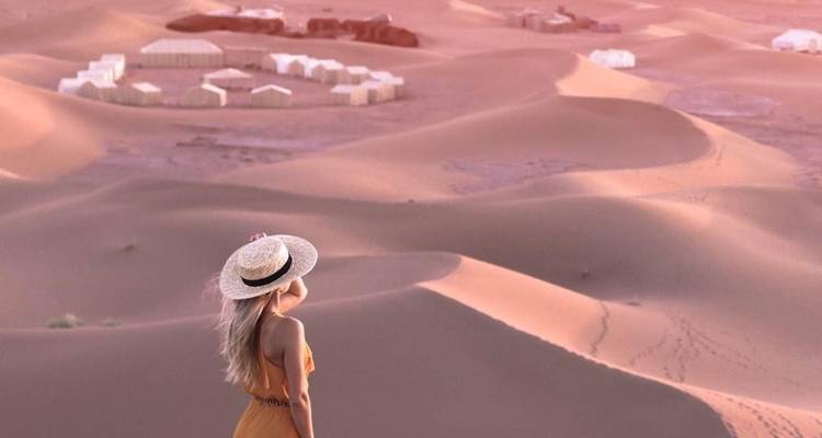 Vrouw die op zandduinen staat en uitkijkt over een woestijnkamp.