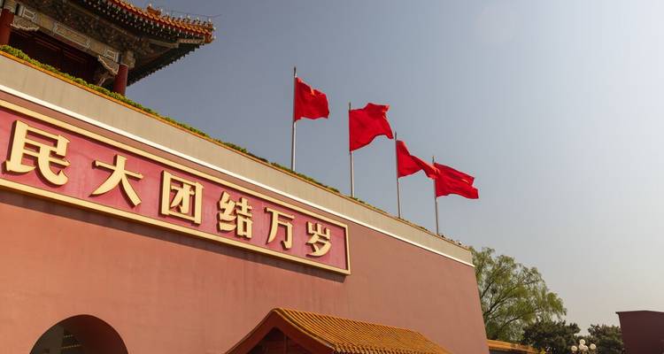 Des drapeaux rouges flottent au sommet de la porte Tiananmen aux murs rouges avec des tuiles de toit dorées sous un ciel bleu brumeux.