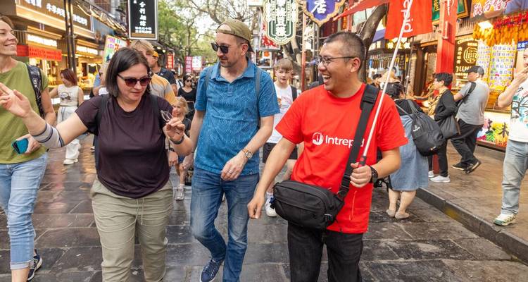 Les voyageurs rient avec leur guide local en se promenant dans une rue piétonne animée éclairée par des lanternes et bordée de stands de nourriture.