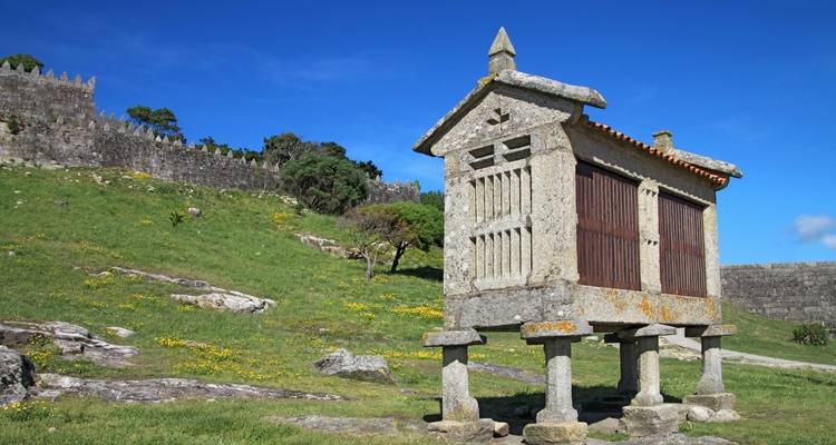 Granero de piedra sobre pilares en un paisaje de hierba.