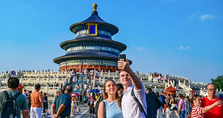 Los turistas se toman selfies frente al Hall of Prayer for Good Harvests circular en el Temple of Heaven bajo un cielo azul brillante.