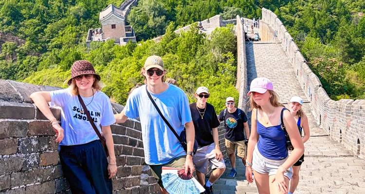 Un grupo de viajeros sube por una sección de piedra de la Gran Muralla con colinas verdes extendiéndose detrás.