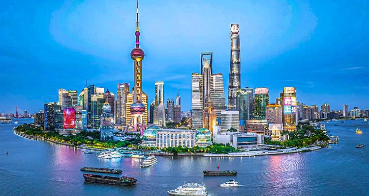 Vista panorámica nocturna del moderno skyline de Shanghai con rascacielos brillantemente iluminados reflejándose en el río Huangpu.
