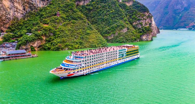 Grand navire de croisière fluviale multi-pont glissant sur les eaux émeraude entre des falaises vertes abruptes.