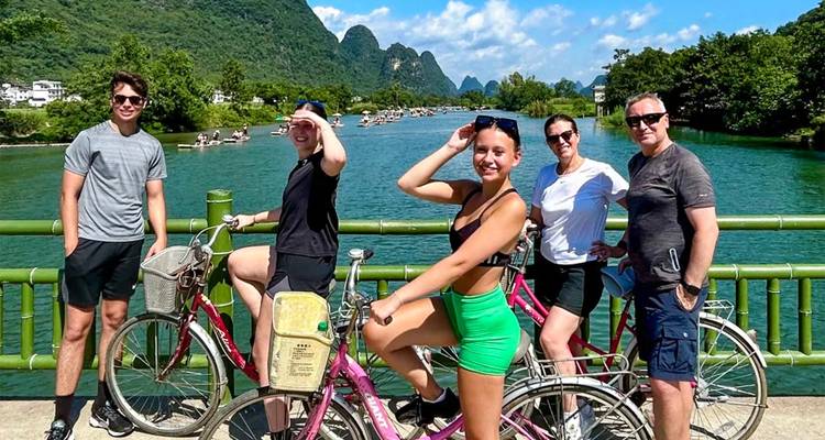 Groupe de cyclistes posant sur un pont enjambant une rivière jade avec des montagnes karstiques en arrière-plan.