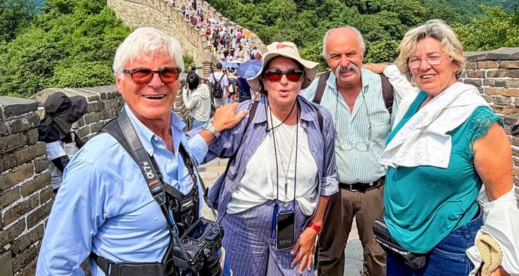 Des voyageurs souriants sur la Grande Muraille de Chine avec des collines verdoyantes en arrière-plan.