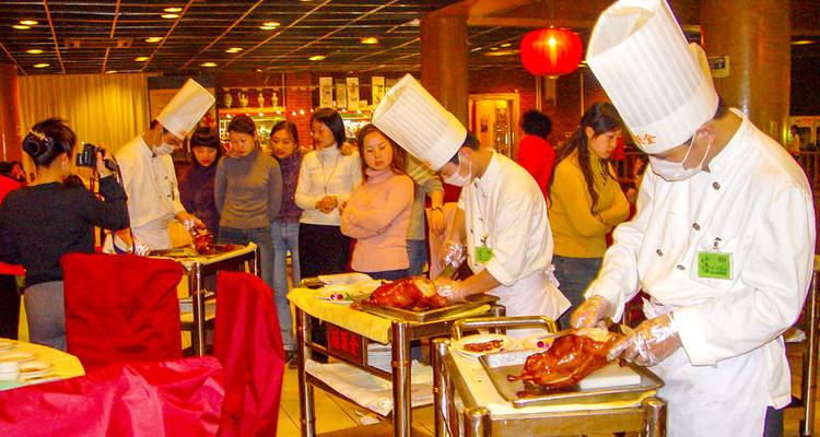 Chefs preparing Peking duck in a restaurant with people watching.