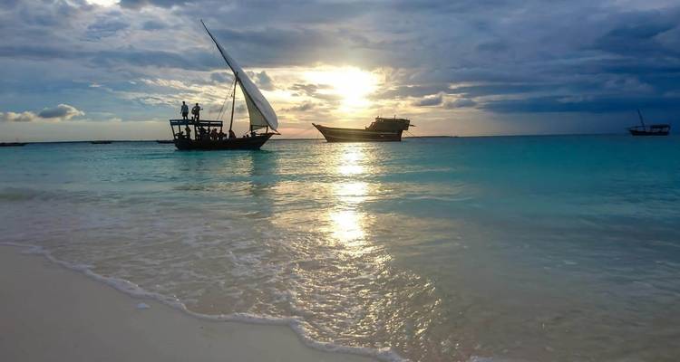 Boote auf türkisem Wasser bei Sonnenuntergang mit sandigem Ufer.