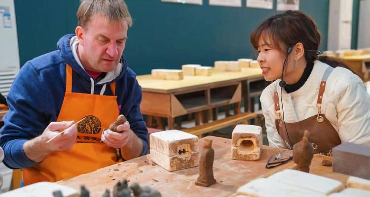Tourist and local instructor shape clay figurines during an indoor pottery workshop.