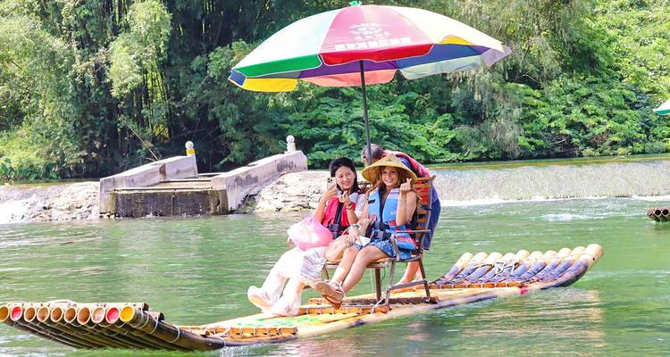 Colorful bamboo raft with parasol carrying smiling travellers along a lush river in Guangxi.