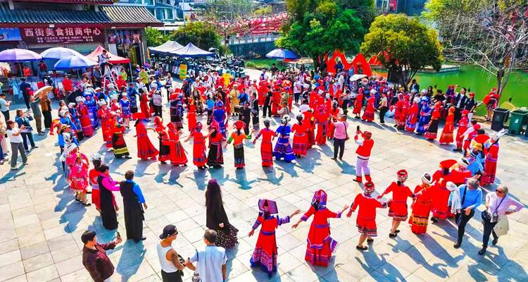 Large circle of people in bright red ethnic dress dancing in a public square during a festival.