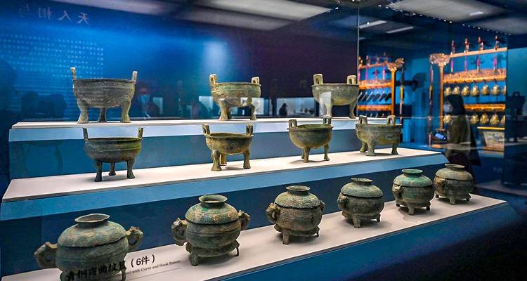 Display cases of ancient bronze vessels showcased in a dimly lit museum gallery.