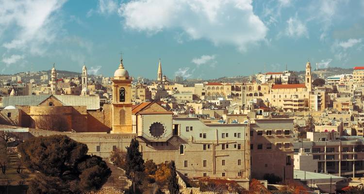 Stadsgezicht met historische kerken en heuvels op de achtergrond.