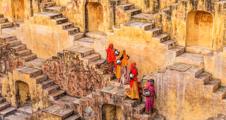 Mujeres con saris de colores brillantes llevando ollas en la escalera antigua de un pozo escalonado amarillo
