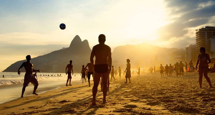 Silhouetten von jungen Menschen spielen bei Sonnenuntergang Strandfu?ball am Strand von Ipanema mit den Gipfeln von Dois Irmãos im Hintergrund.