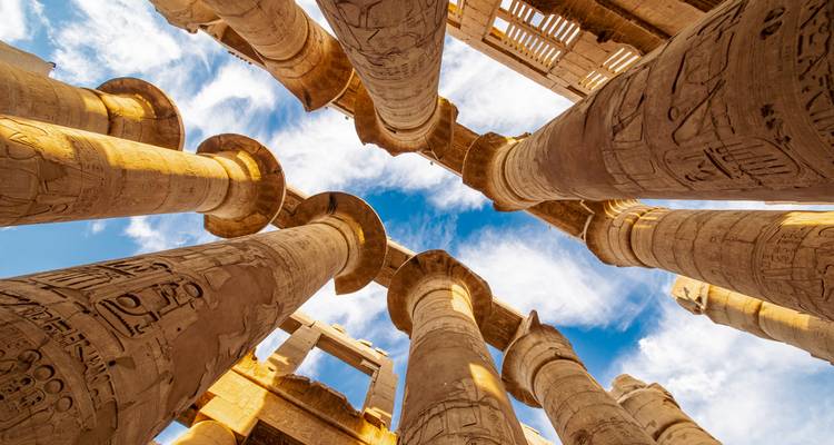 Perspectiva hacia arriba de las enormes columnas cubiertas de jeroglíficos del Templo de Karnak contra un cielo azul vibrante