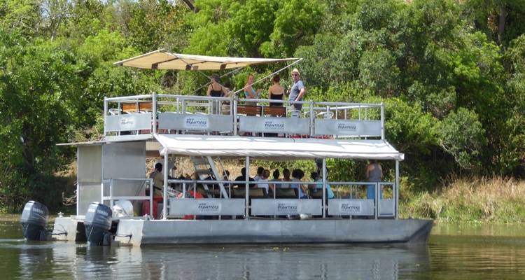 A large boat on a river with people on board, surrounded by greenery.