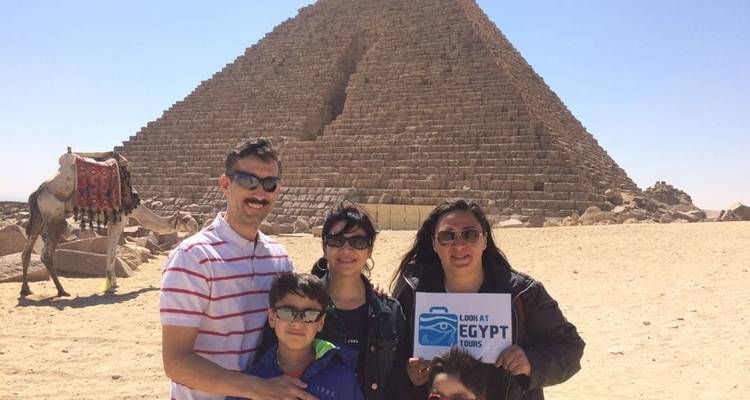 Family posing with pyramids in Egypt holding a tour sign.
