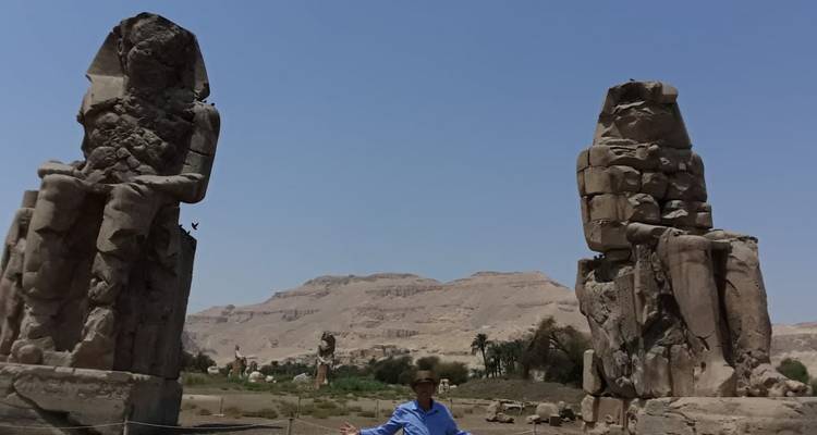 Een man die tussen de Colossi van Memnon staat.