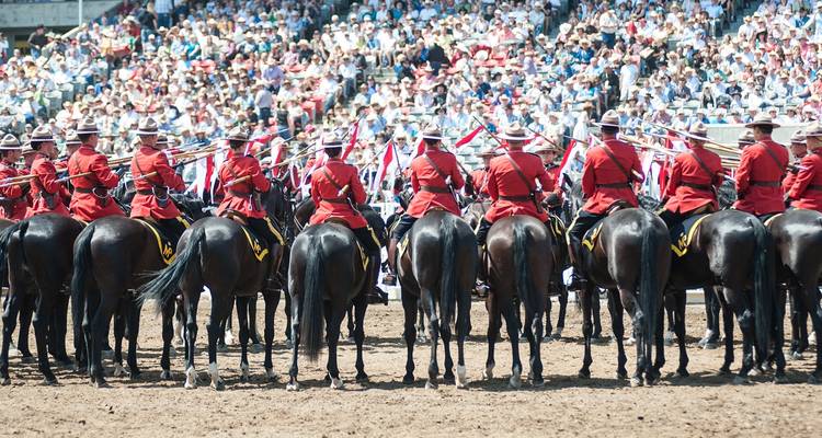Policía Montada Real Canadiense en uniformes rojos a caballo actuando ante una gran multitud sentada