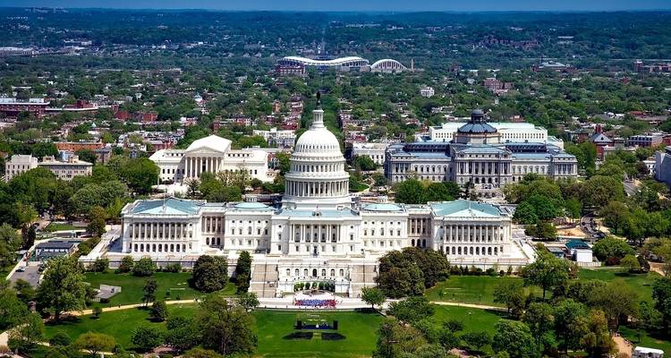 Aerial view of the United States Capitol surrounded by various buildings and greenery.