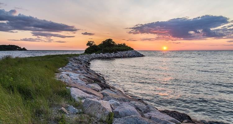 Sunset over a rocky coastline with vibrant colors in the sky.