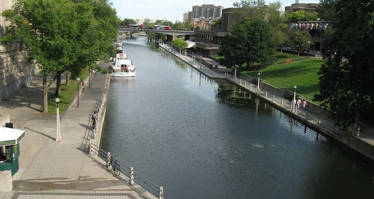 View of a canal with boats and people walking alongside on a sunny day.