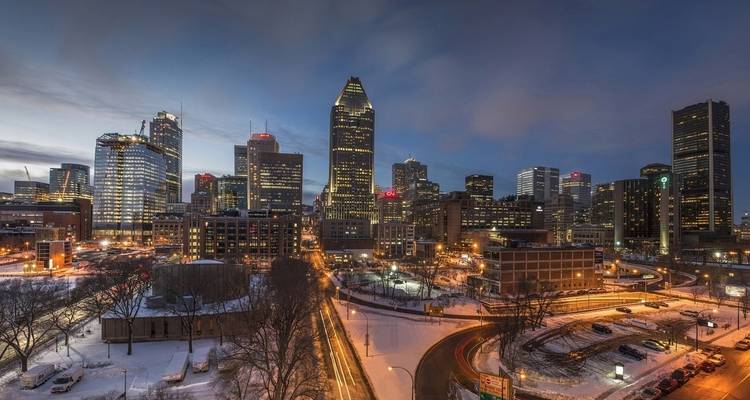 Montreal cityscape at dusk with snowy rooftops and illuminated buildings.