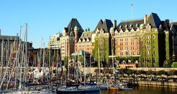 Historic ivy-clad hotel overlooks a harbour crowded with sailboats on a sunny day.