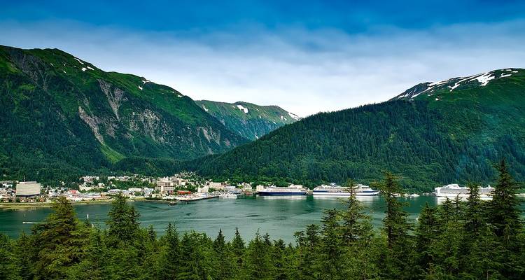 Coastal Alaskan town nestled between lush green mountains and a bay filled with cruise ships.