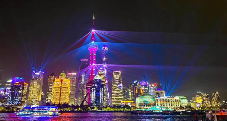Panorama nocturno del Bund con los rascacielos de Shanghai iluminados con luces láser de colores sobre el río