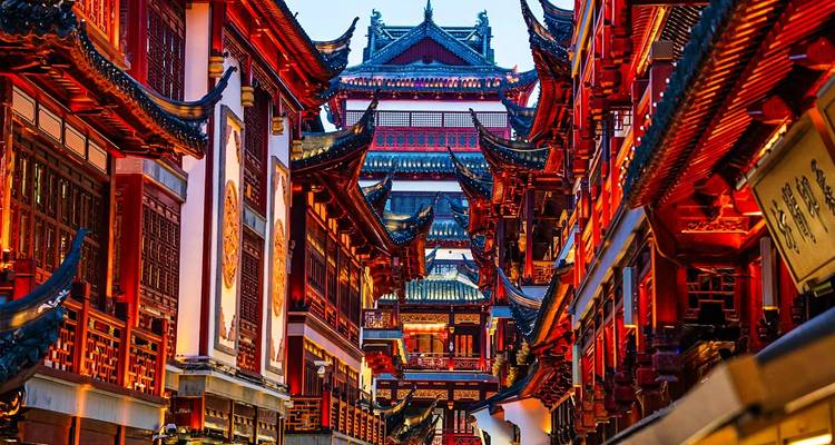 Callejón estrecho de tradicionales edificios rojos de Shanghái con techos ornamentados brillando bajo la luz del atardecer