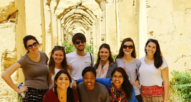 Group of people in front of an arched hallway with smiling faces.