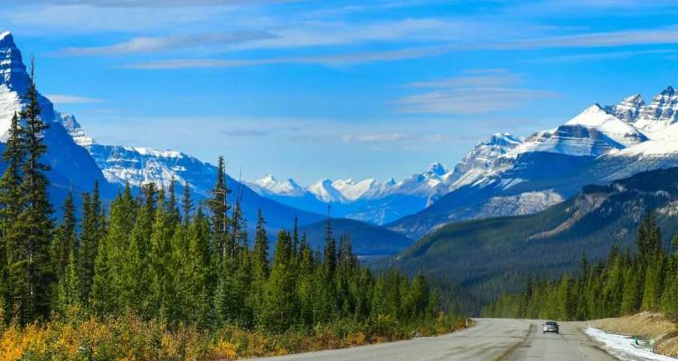 Een lange weg slingert door eeuwiggroene bossen naar sneeuwbedekte bergtoppen langs Canadas Icefields Parkway.