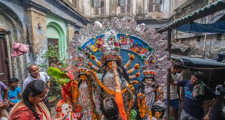 People offering prayer to a colorful Hindu idol in a courtyard.